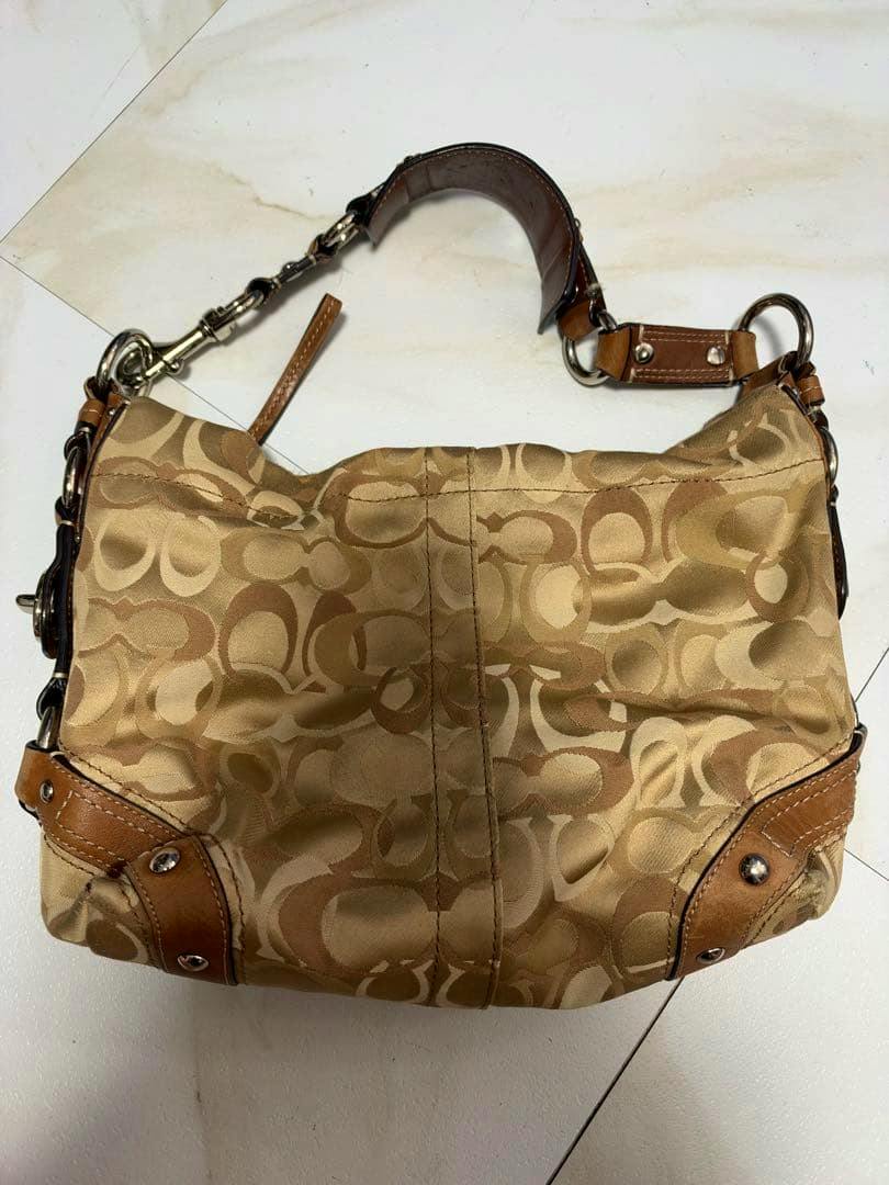 Beige Coach signature-patterned handbag shown lying flat with visible leather trim and shoulder strap.