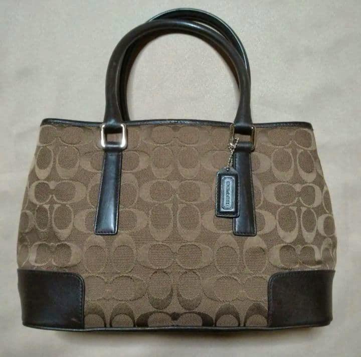 Brown COACH signature canvas handbag with dark leather handles, corner trim, and a Coach hangtag.