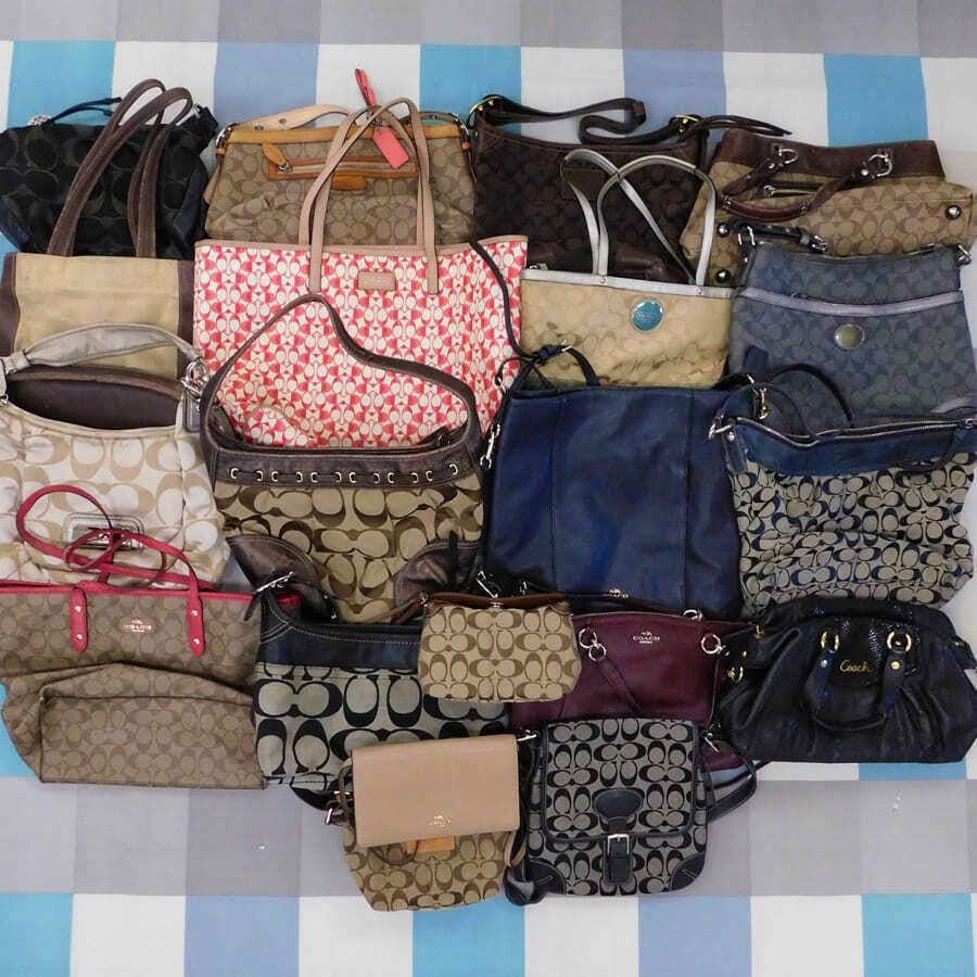 A collection of Coach handbags in various colors and signature "C" patterns arranged together on a surface.