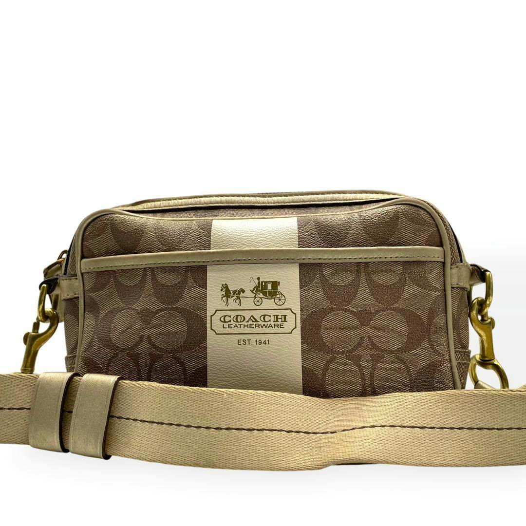 Front view of a Coach signature canvas shoulder bag with a cream center stripe and beige strap.