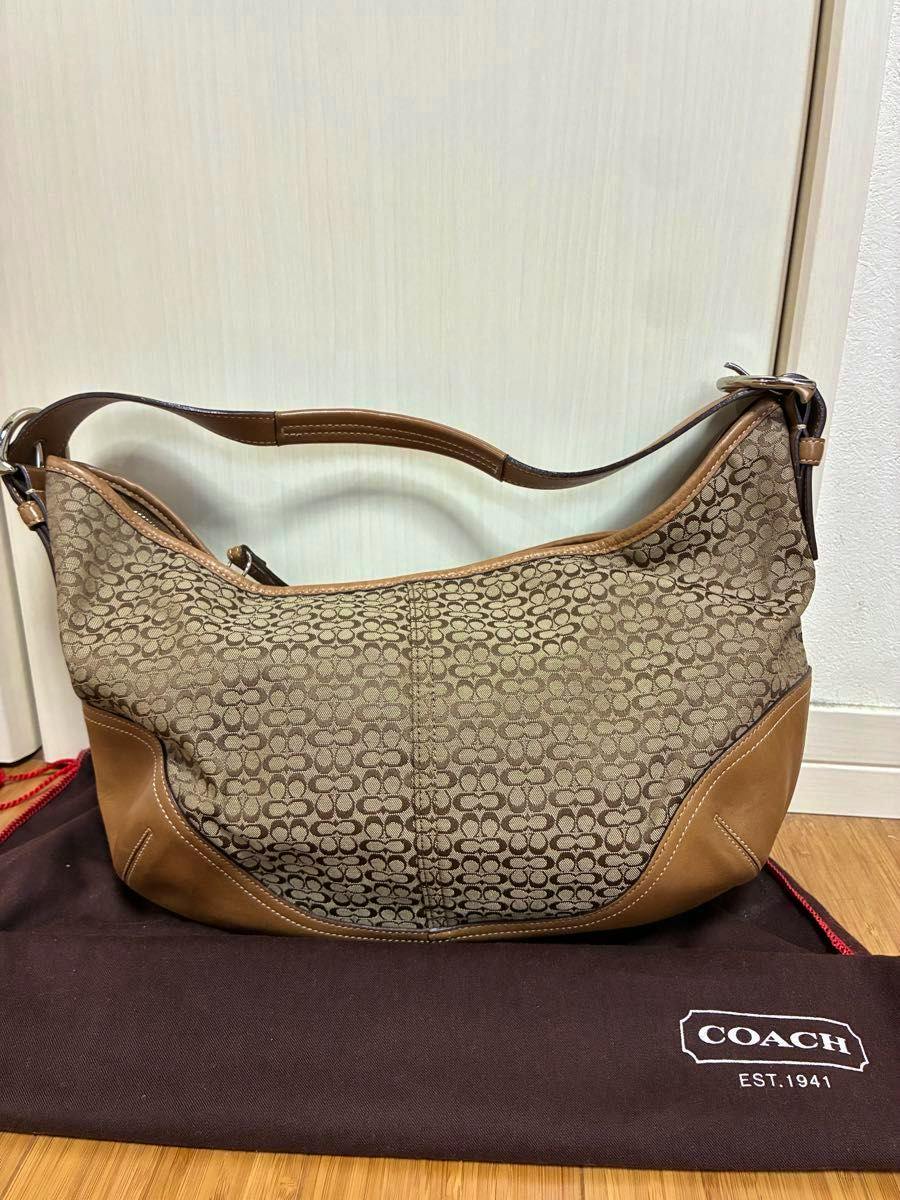 Front view of the Coach signature canvas hobo shoulder bag with brown leather trim resting on a Coach dust bag.
