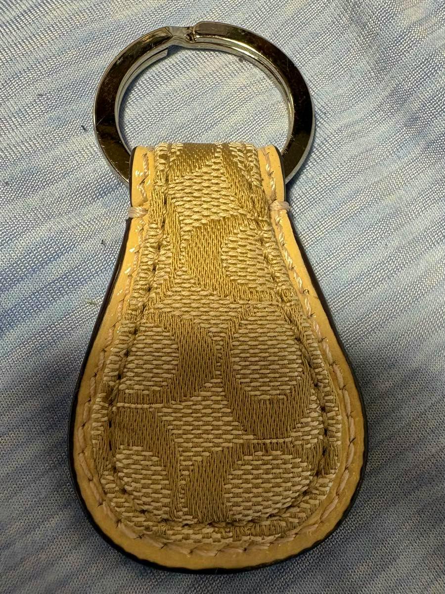 Teardrop-shaped Coach signature fabric keyring bag charm with a metal key ring on a cloth background.