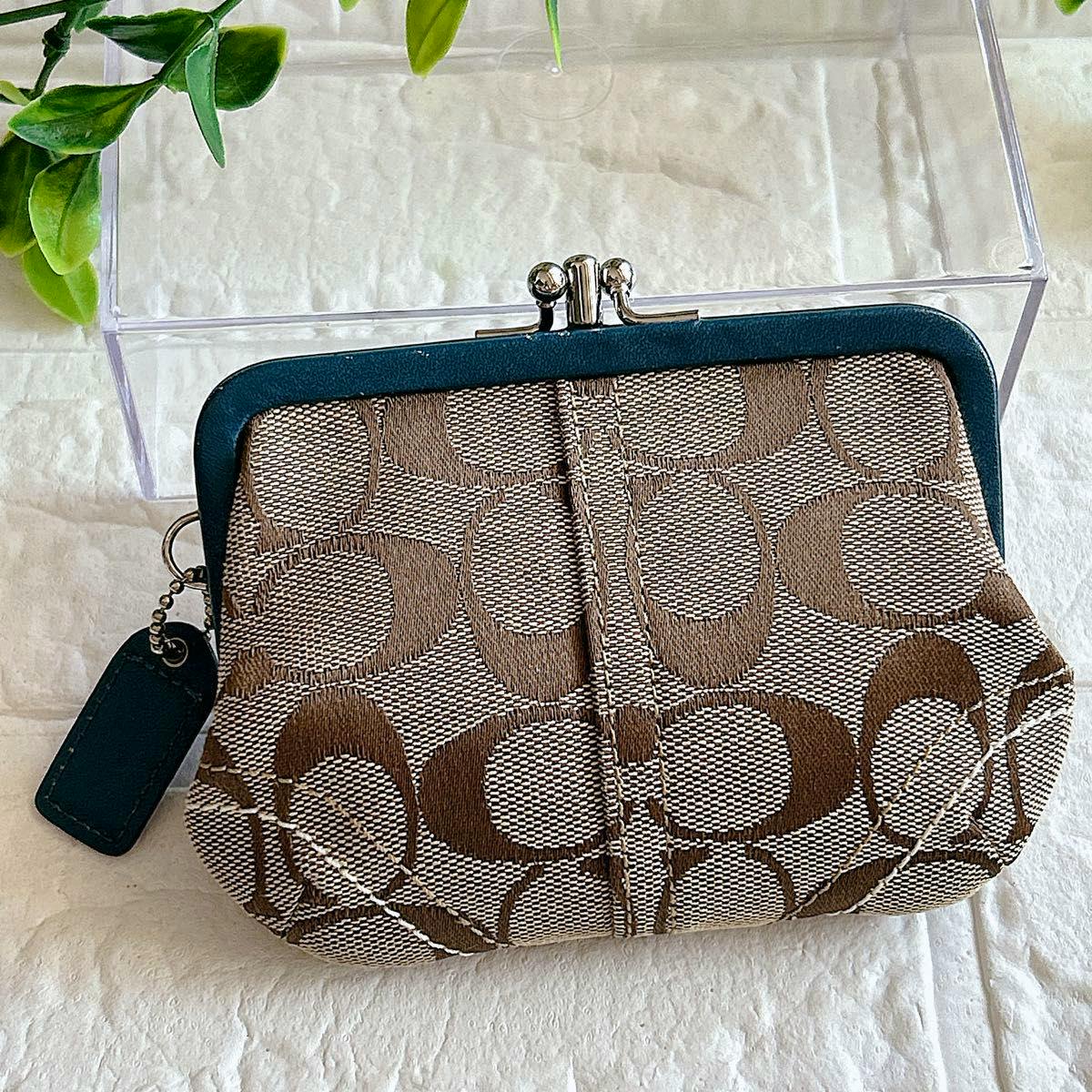 Coach signature canvas kisslock coin case showing the brown 'C' pattern, teal leather trim with a Coach tag, and a silver kisslock clasp.