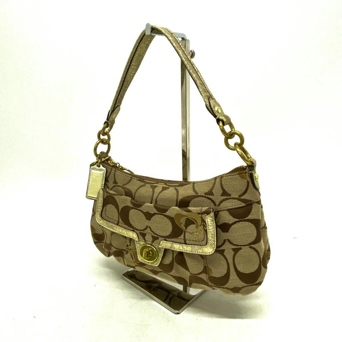 Front view of a brown Coach signature canvas handbag with gold hardware and a single shoulder strap displayed on a stand.