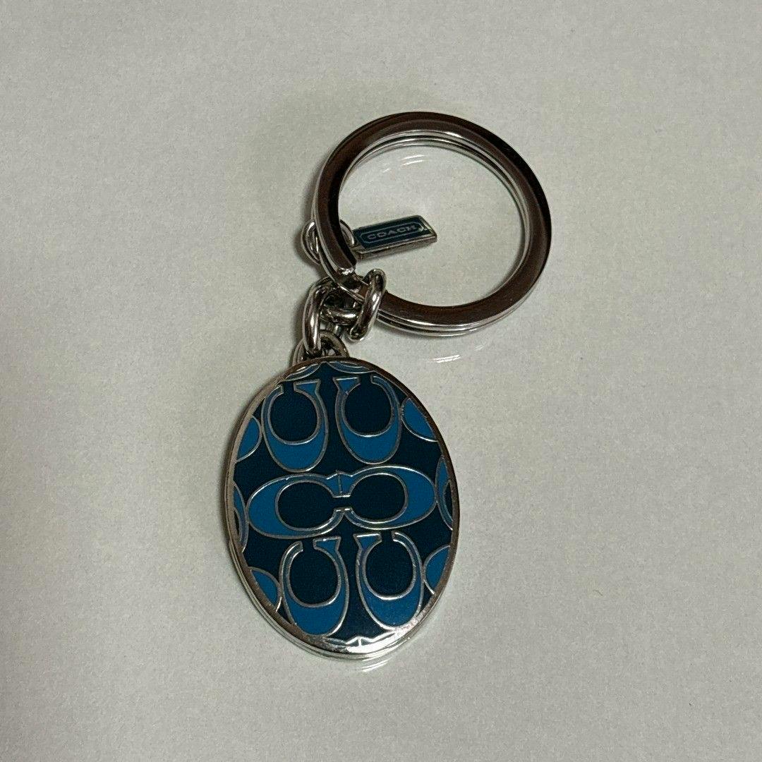 Oval blue Coach keychain pendant with signature pattern attached to a silver key ring.