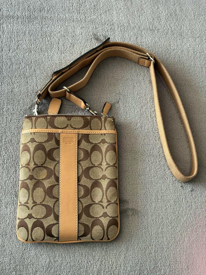 Beige Coach signature canvas shoulder bag with a leather center stripe and matching strap laid flat on a gray surface.