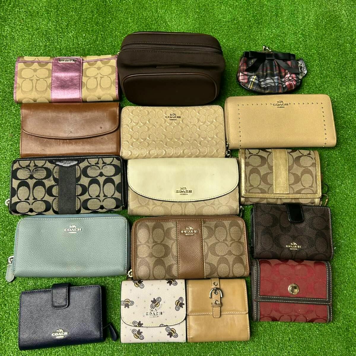Overhead photo of multiple COACH wallets and small accessories arranged on a green grass-like surface, showing various colors and signature patterns.