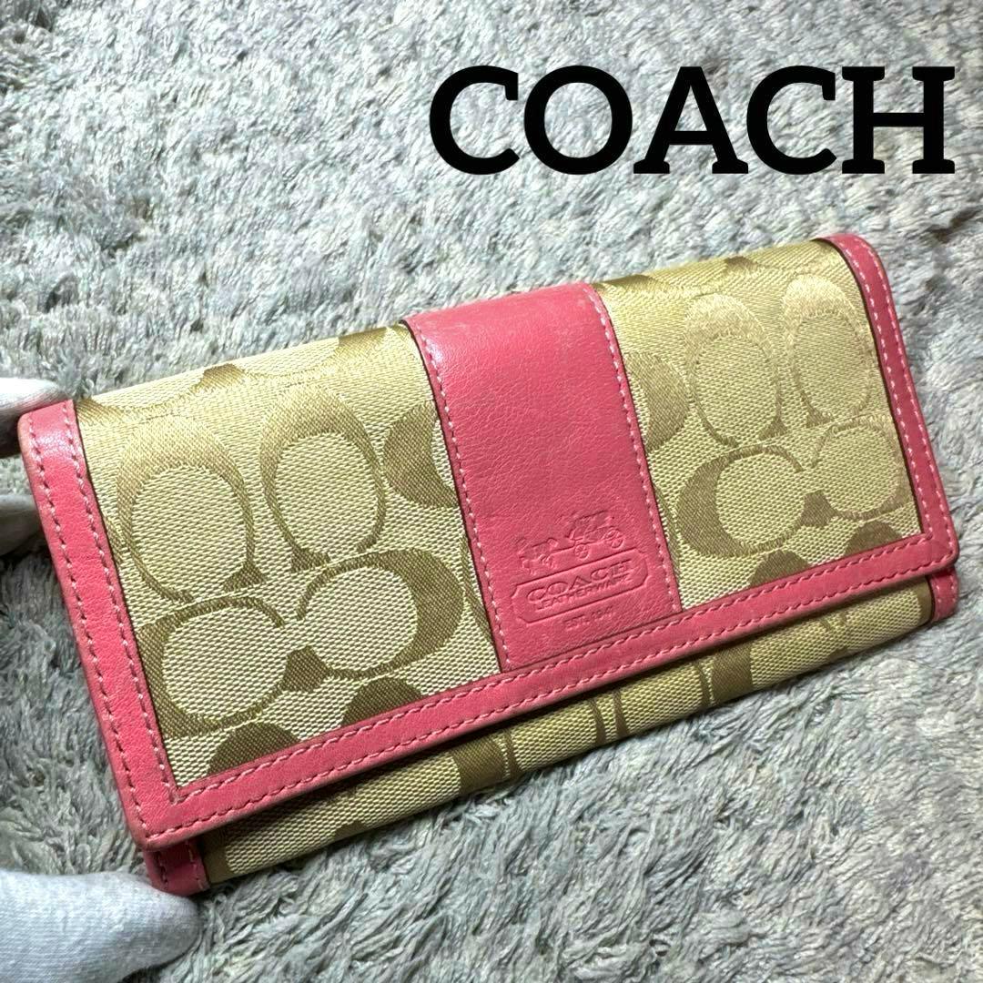 Closed Coach signature beige canvas long wallet with pink leather trim shown on a gray textured surface.