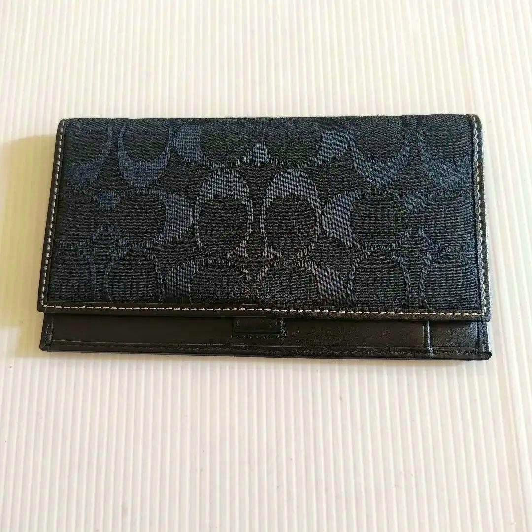 Black Coach signature canvas long wallet shown closed on a white ribbed background.