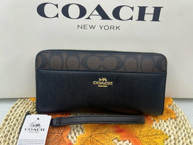 Front view of a COACH zip-around long wallet in signature canvas and black pebbled leather with gold COACH logo and wrist strap, shown against a COACH box.