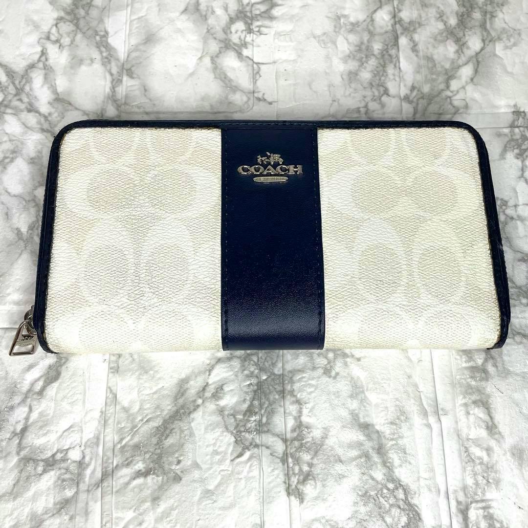 White and navy Coach signature long wallet with a central navy leather stripe and metal COACH logo resting on a marble background.
