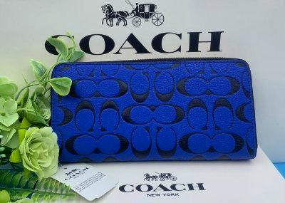 Blue Coach signature long-zip synthetic leather wallet displayed with a Coach logo backdrop and product tag.
