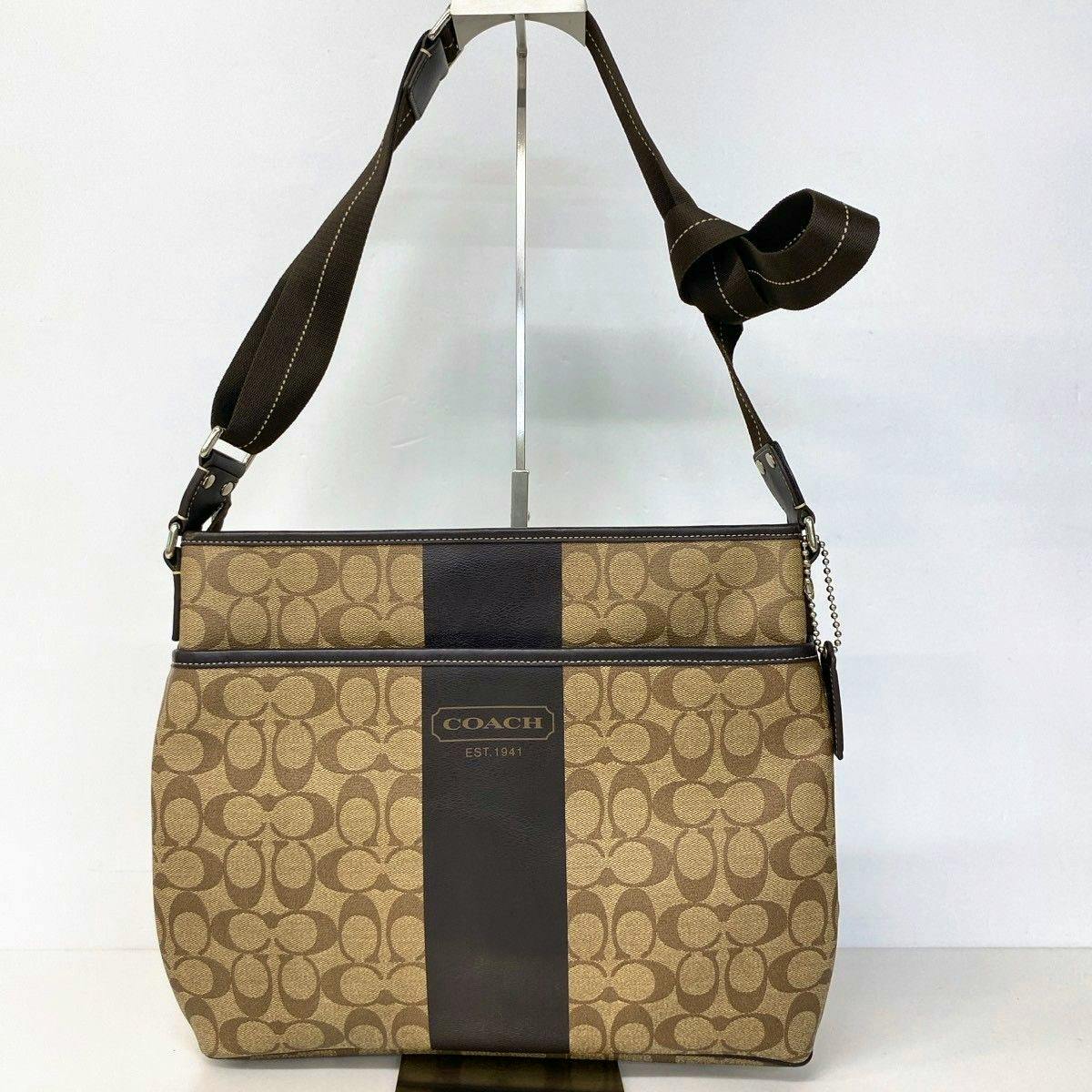 Front view of the brown Coach signature canvas shoulder bag with a central dark vertical stripe and adjustable brown strap.