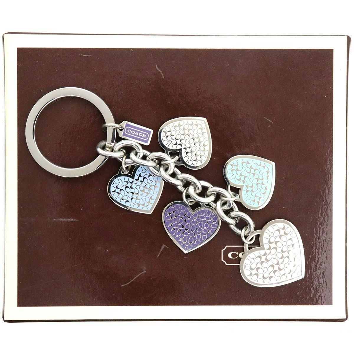 Coach metal bag charm keyring with five heart-shaped charms displayed on a brown Coach box.