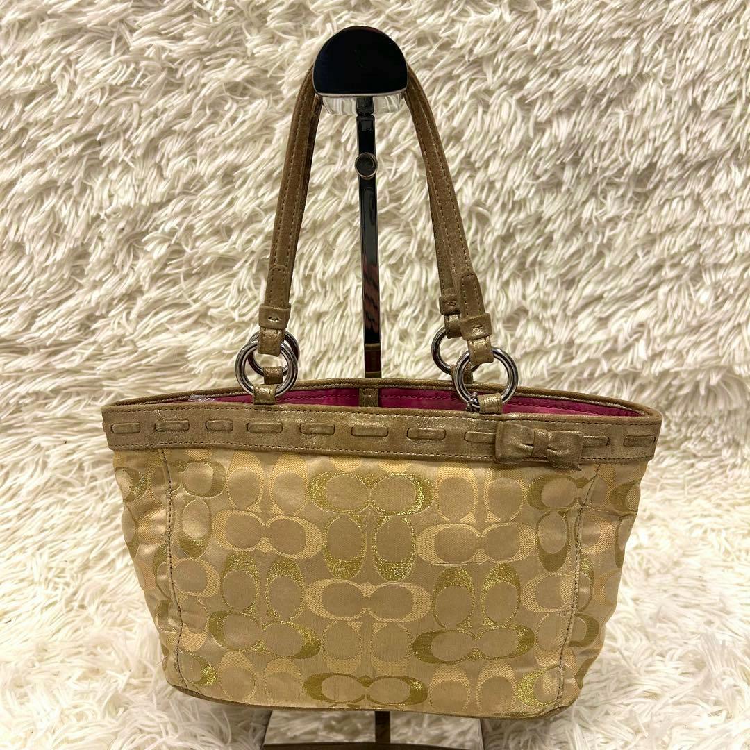 Coach signature mini handbag in beige canvas with repeating 'C' pattern and two handles displayed on a stand.