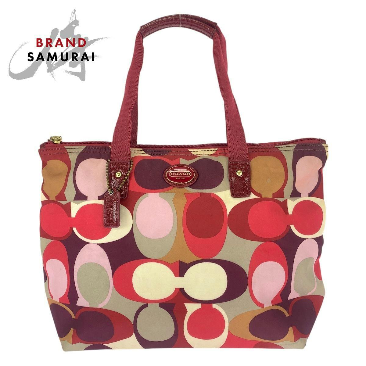 Front view of a multicolor Coach signature nylon and leather tote bag with red handles and gold hardware.