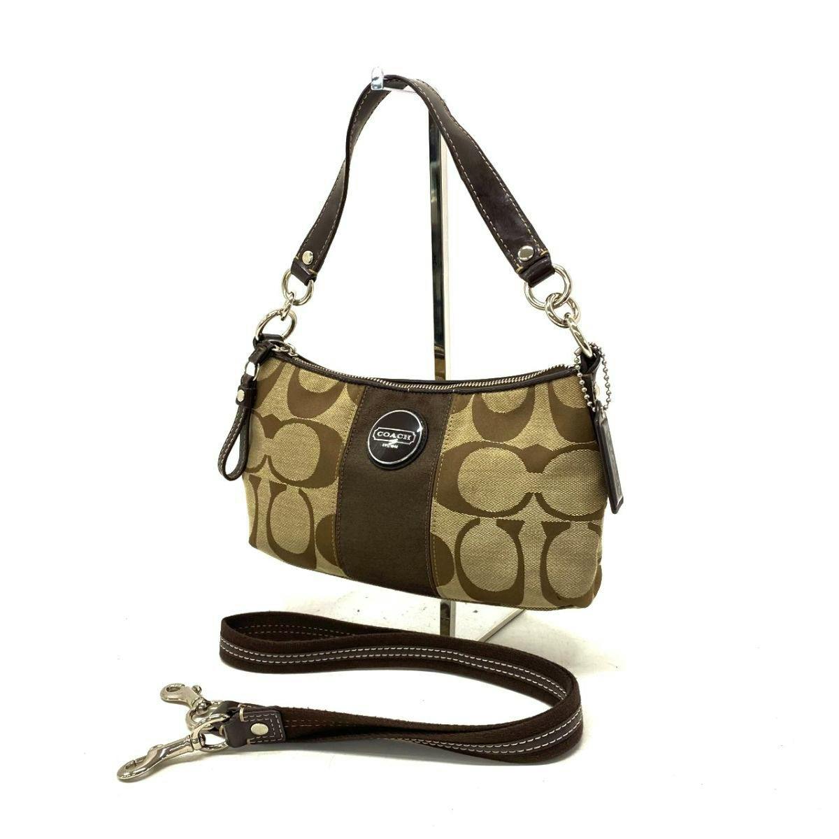 Coach signature canvas shoulder bag with leather center panel and detachable leather strap displayed on a stand.