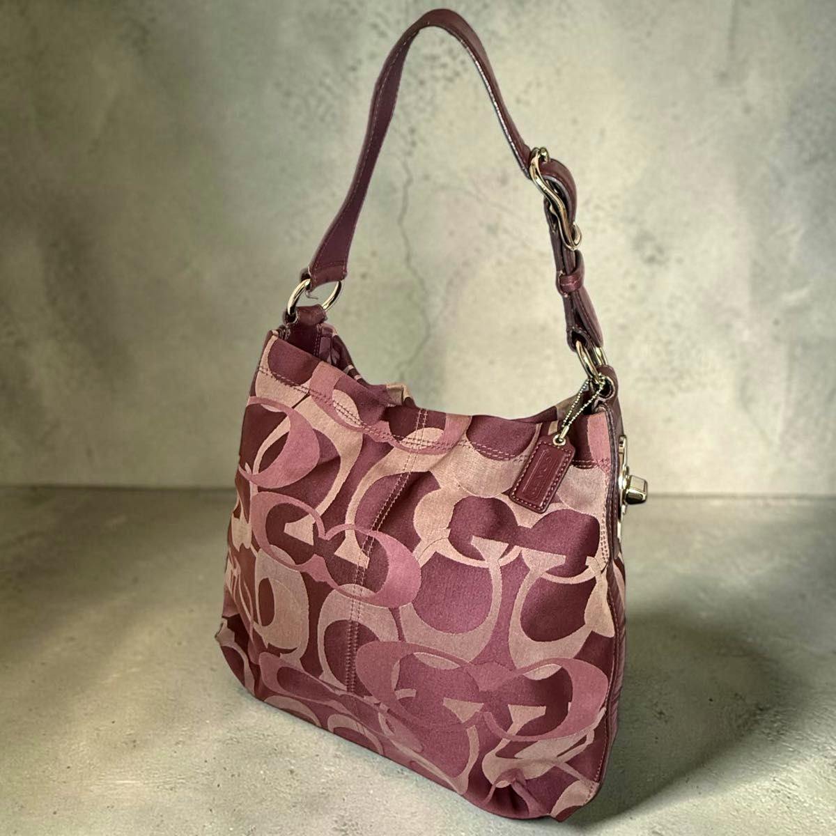 COACH signature one-shoulder bag in pink tones with large C pattern and a single shoulder strap shown angled on a neutral background.
