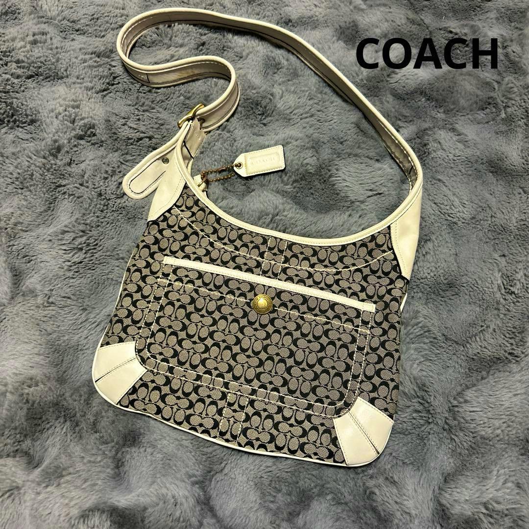 Front view of a Coach signature canvas one-shoulder bag with light leather trim on a gray background.