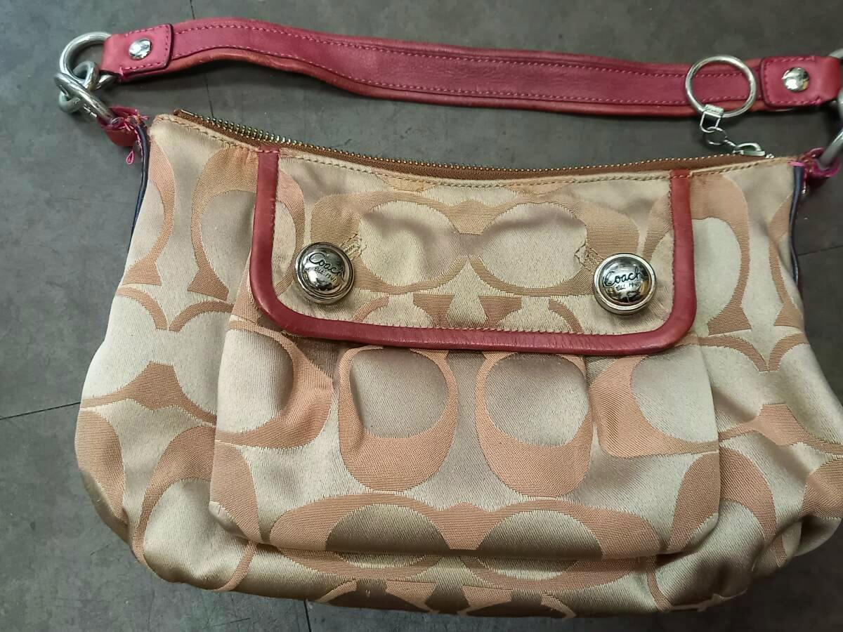 Front view of the beige and pink Coach signature canvas one-shoulder bag with pink leather trim, visible strap, and front flap with Coach buttons.