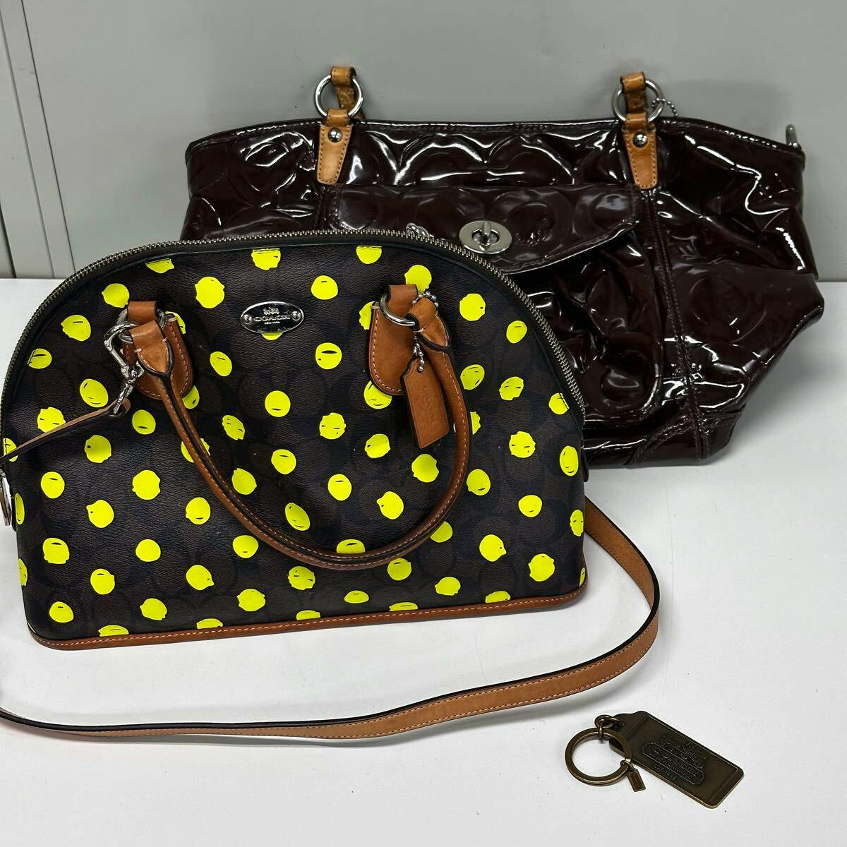 Two Coach bags (a black dome-shaped bag with yellow polka dots and a dark brown patent leather tote) with a Coach keychain placed nearby.