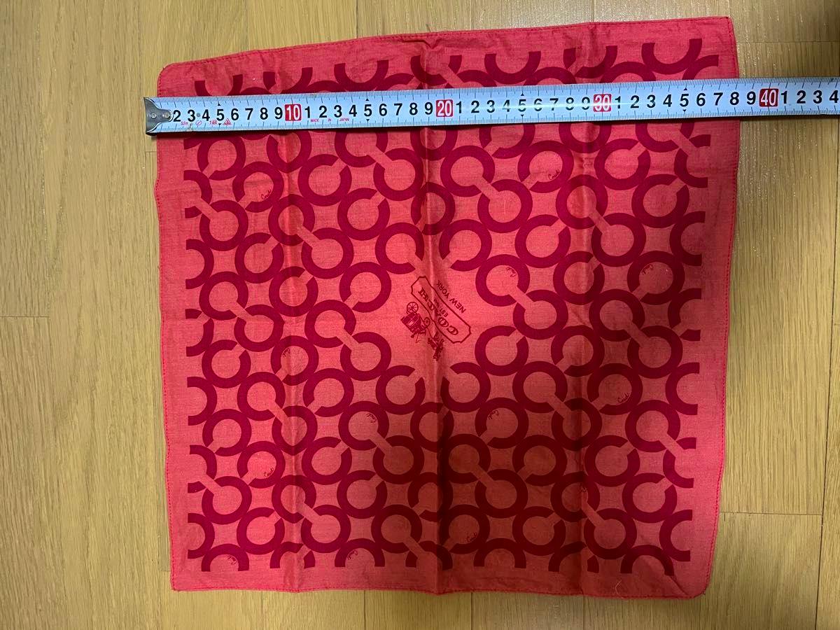 A red COACH signature-pattern cotton handkerchief laid flat on a wooden floor with a measuring tape across the top.