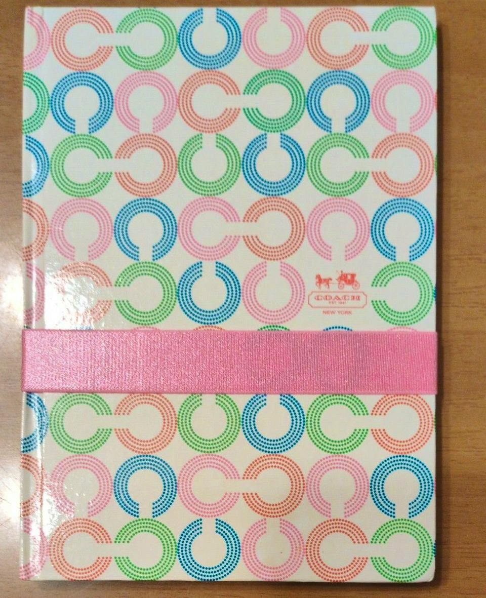 Front cover of a COACH notebook showing a multicolor signature-style circle pattern and a horizontal pink band.