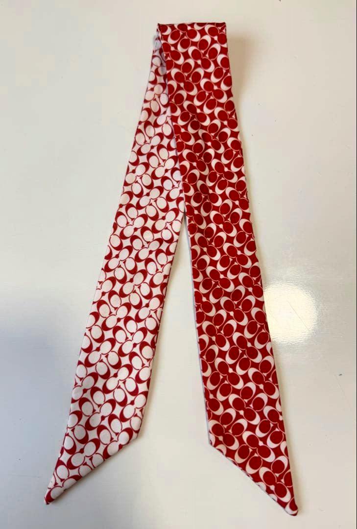 A red and white Coach signature-pattern skinny scarf laid flat on a white background.