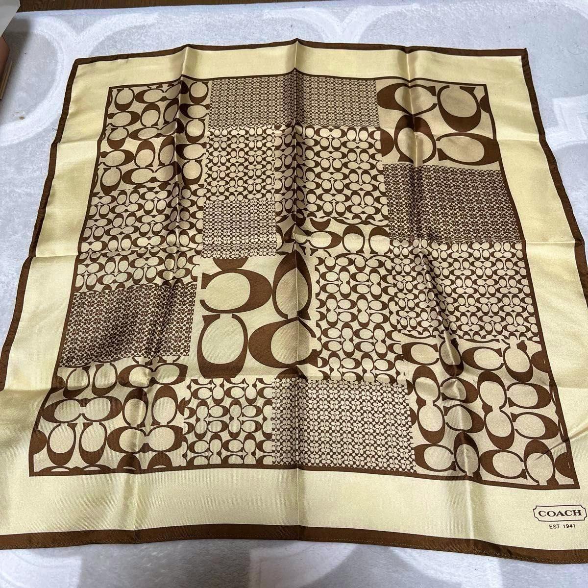 Brown and beige COACH signature-pattern polyester scarf laid flat showing patchwork C logo design and COACH label in the corner.
