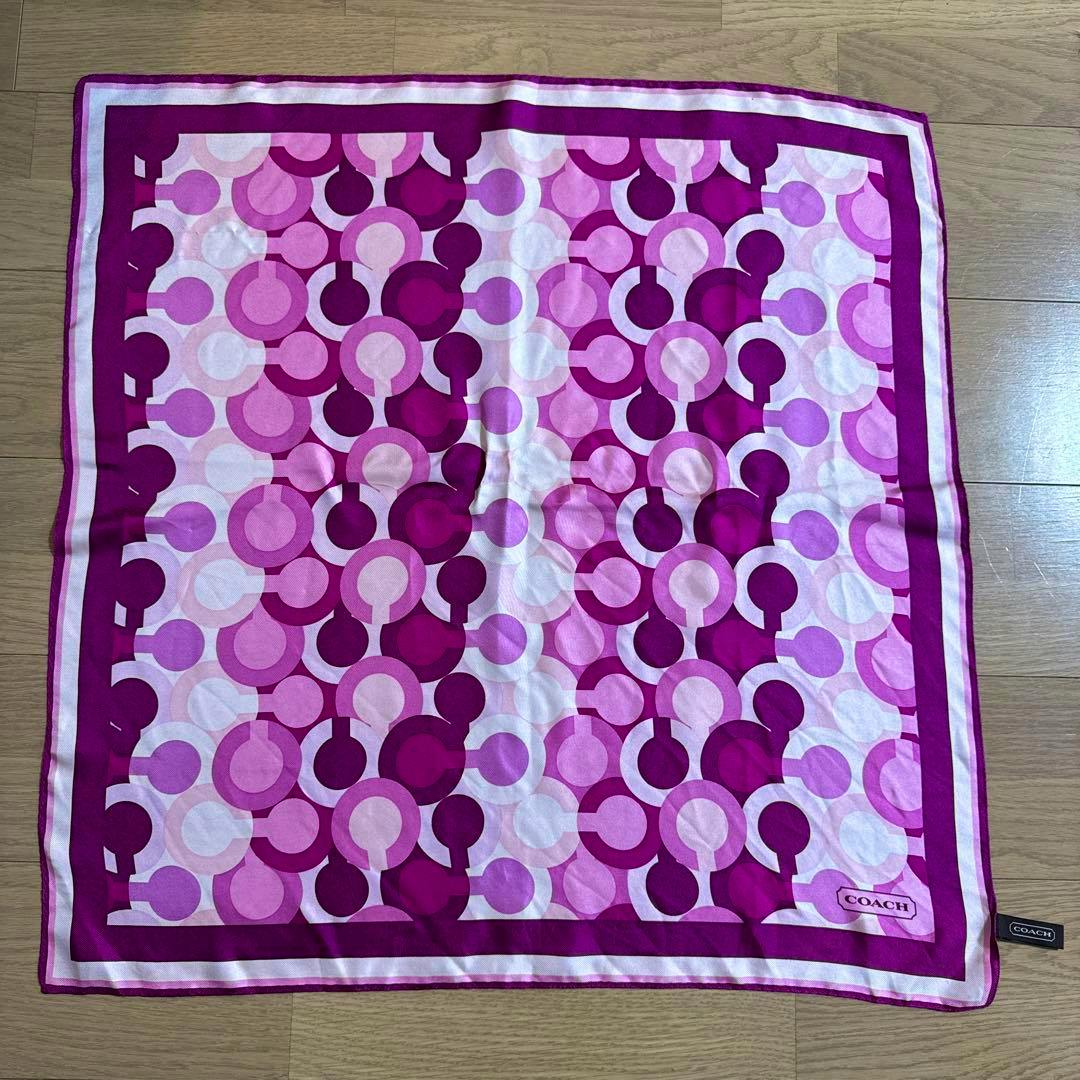 Purple Coach signature-pattern silk scarf laid flat on a wooden floor showing the circular print and border.