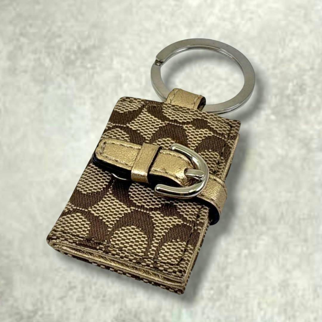 Coach signature photo-frame bag charm key holder with brown and beige signature pattern, a gold-tone buckle detail, and a metal key ring.