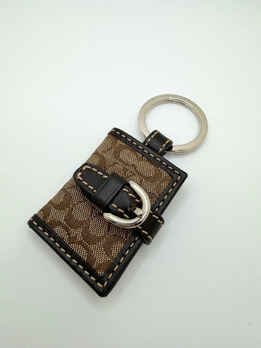 Brown Coach signature fabric bag charm key holder with leather trim, buckle detail, and metal key ring on a white background.