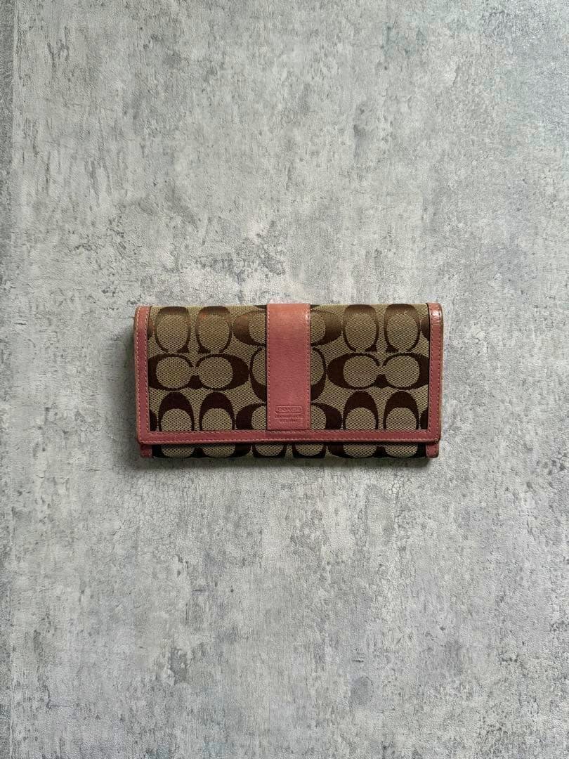 Front view of a Coach signature canvas wallet with pink trim placed on a gray textured surface.