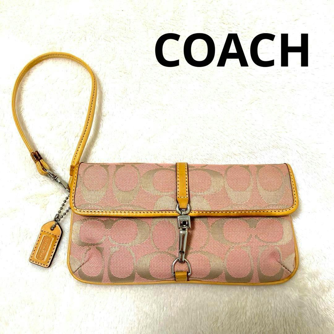 Pink COACH signature canvas pouch wristlet with tan leather trim, metal clasp, and a detachable wrist strap on a white background.
