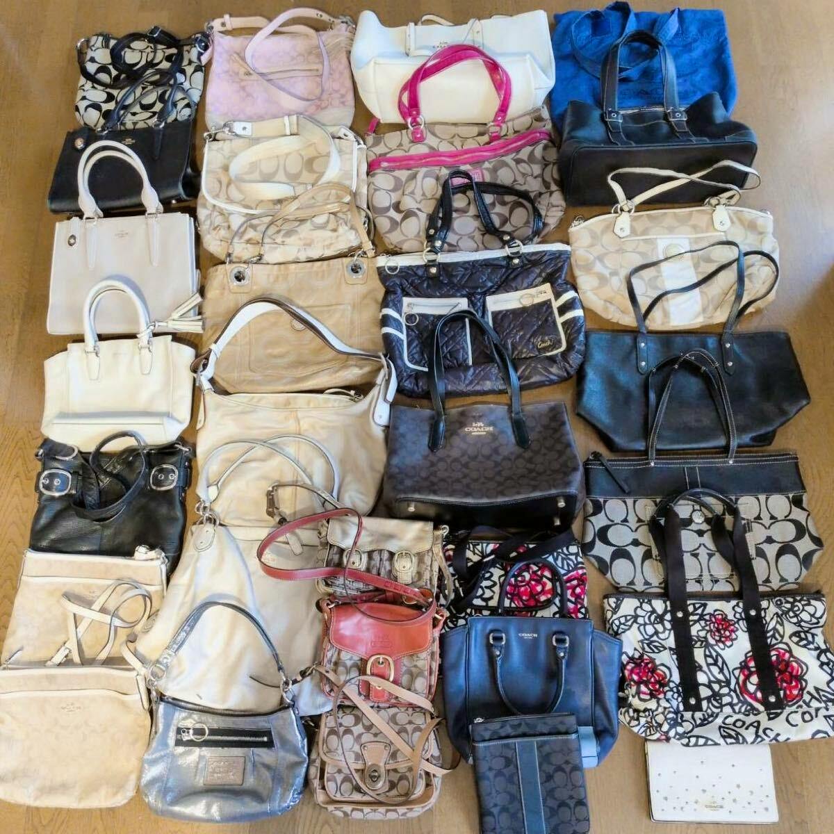 A large assortment of Coach canvas and leather handbags, tote bags, and shoulder bags laid out on a wooden floor.