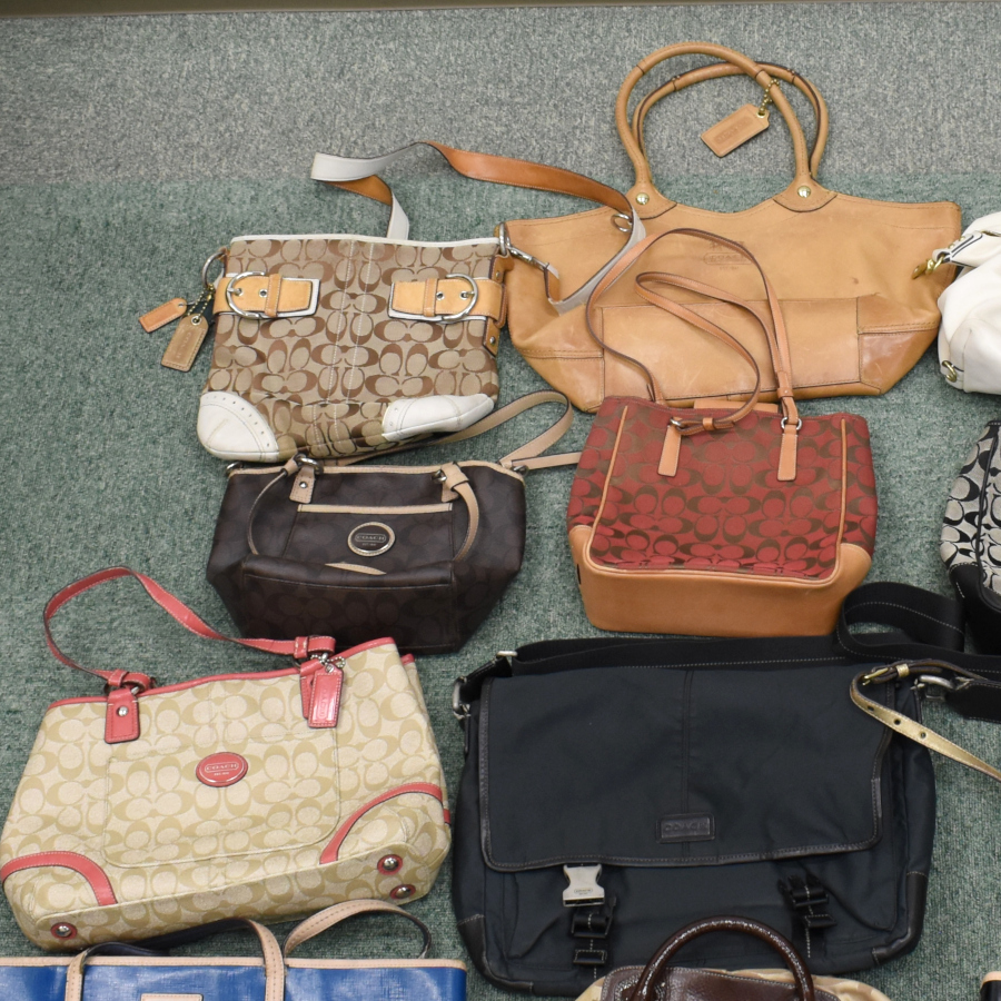 Several handbags and shoulder bags, including Coach signature patterned bags, arranged on a carpeted floor.