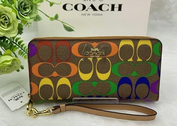 Front view of a COACH long zip-around signature canvas wallet with rainbow C pattern and detachable wrist strap.