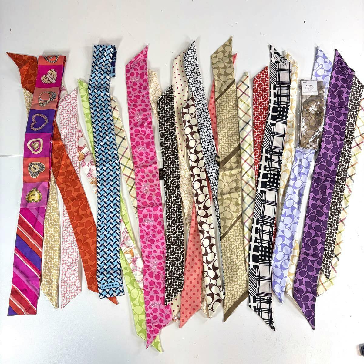 Multiple narrow ribbon-style silk scarves with Coach signature patterns and varied colors laid flat on a white background.