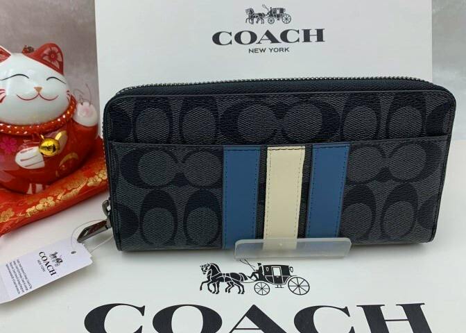 Front exterior of a Coach signature canvas long-zip wallet with blue and cream center stripes, displayed in front of a COACH box.