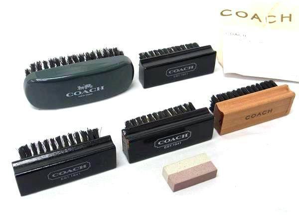 A set of five COACH shoe cleaning brushes and a small eraser displayed on a white background.