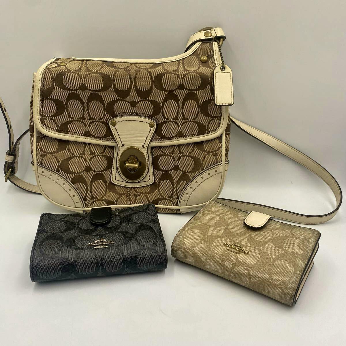 Coach signature canvas shoulder bag with white trim and two Coach signature canvas wallets displayed in front.