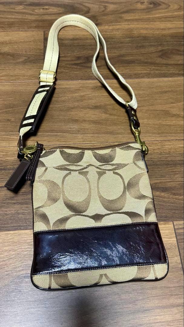 Beige and brown COACH signature canvas shoulder bag laid flat, front view showing leather trim and adjustable strap.