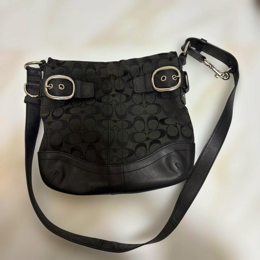 Black Coach signature canvas shoulder bag with leather trim, silver buckles, and an adjustable strap laid flat on a white background.