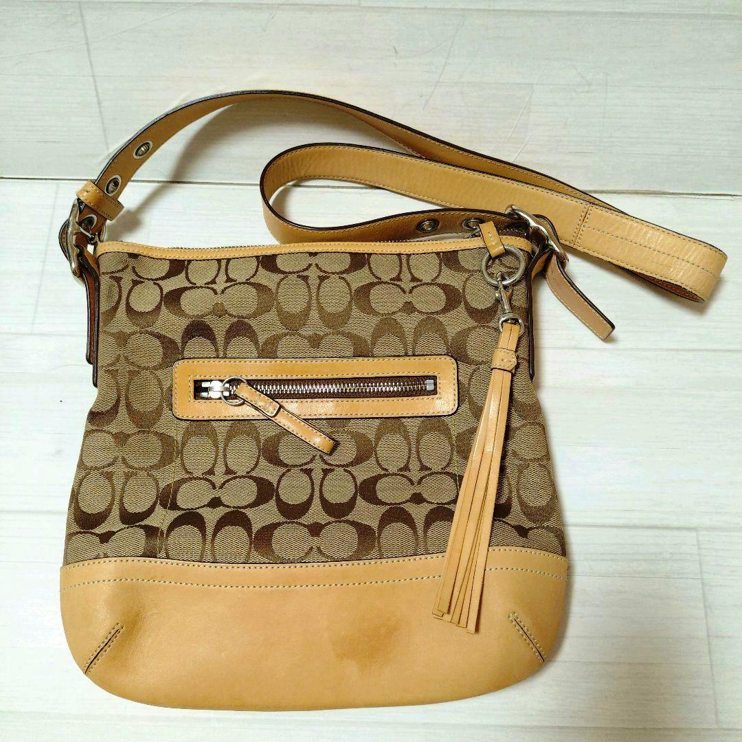 Brown COACH signature canvas shoulder bag with tan leather trim, front zip pocket, tassel, and shoulder strap.