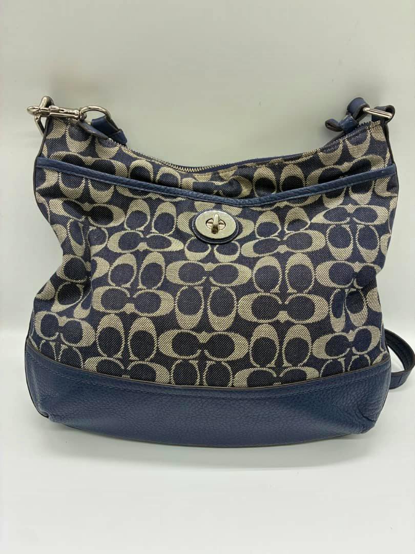 Navy Coach signature canvas shoulder bag shown from the front with signature C pattern, leather base, and metal turn-lock closure.