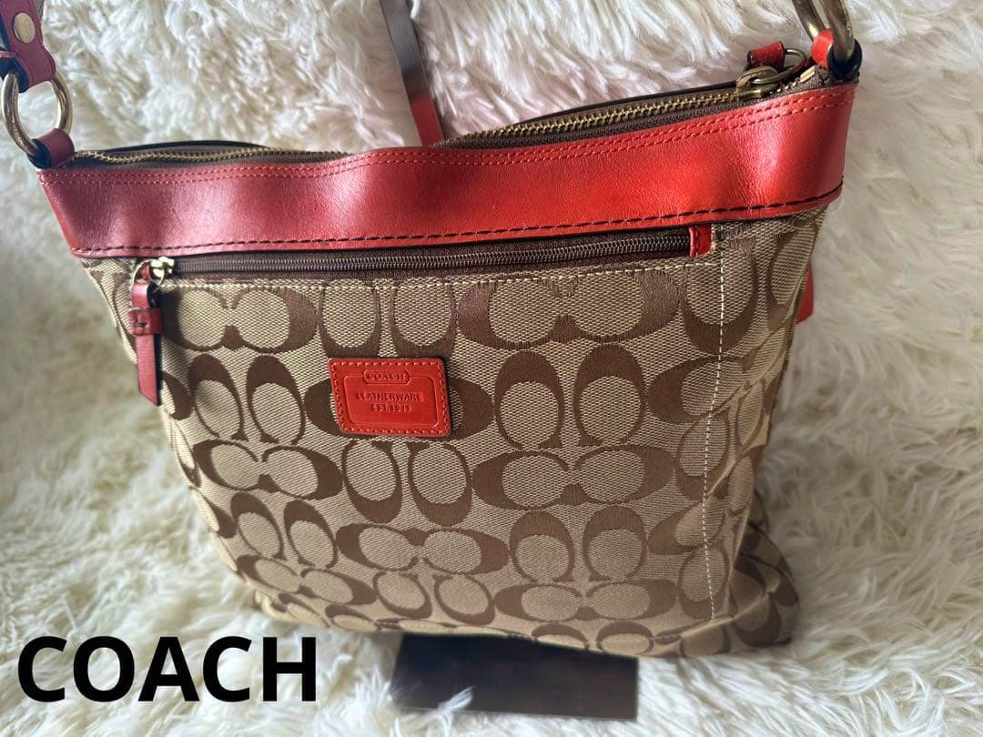 Front view of the Coach signature canvas shoulder bag in reddish-orange and beige showing the logo patch and front zip pocket.