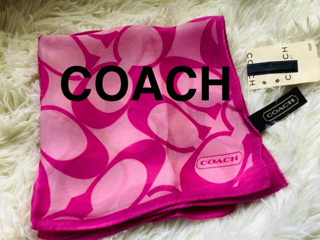 Folded pink COACH silk chiffon scarf showing the signature pattern and attached tags on a white fur surface.