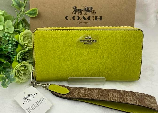 Yellow-green Coach long wallet with a detachable strap and tag displayed in front of a Coach box.