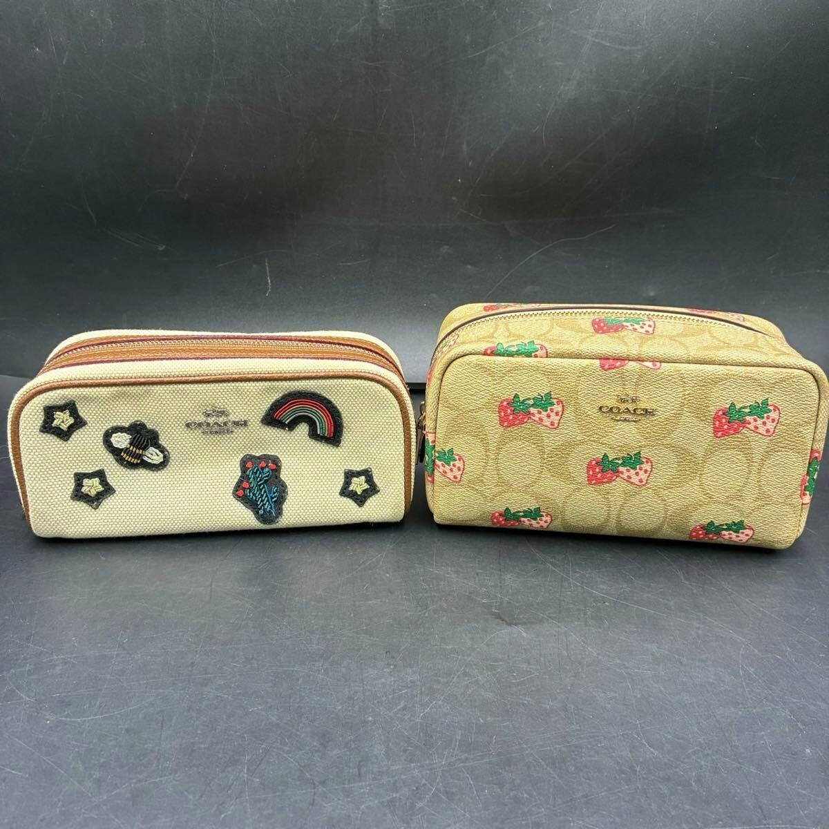 Two COACH canvas pouches displayed side by side, one with strawberry print and one with embroidered patches.