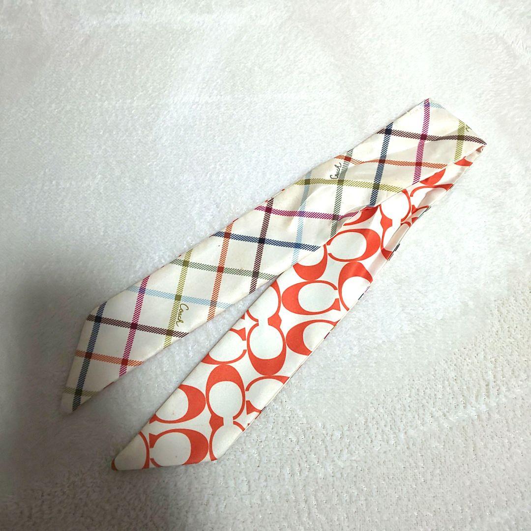 A Coach silk scarf with orange signature 'C' pattern on one side and multicolored plaid on the other, laid flat on a white surface.